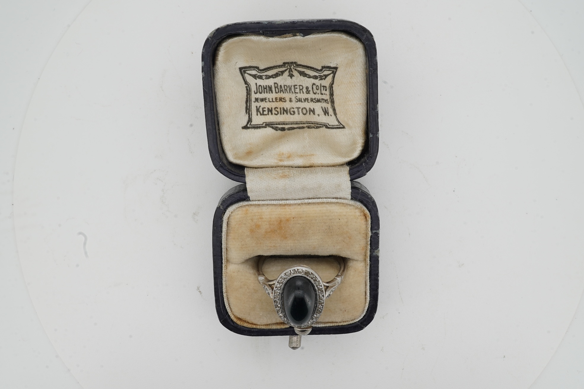 A sapphire and diamond ring, 1920s, set with a cabochon sapphire measuring approximately 2.4 x 6.8 x 4.7mm, within a border of rose-cut diamonds, mounted in platinum, size L1/2